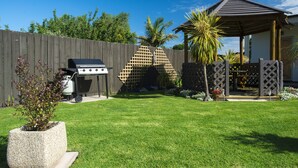 A backyard with a wooden fence, a grill, a palm tree, and a gazebo. - Alfresco Motor Lodge (Gisborne)
