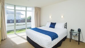 A bedroom with a large bed, a glass door leading to a balcony, and a small table with a phone and a lamp. - Alfresco Motor Lodge (Gisborne)