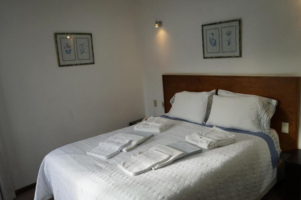 Un lit bien fait, avec du linge de lit et des serviettes blanches, une tête de lit en bois et deux tableaux encadrés accrochés au mur.