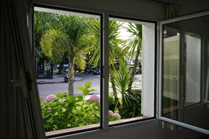 A room with a view of a street and greenery outside.