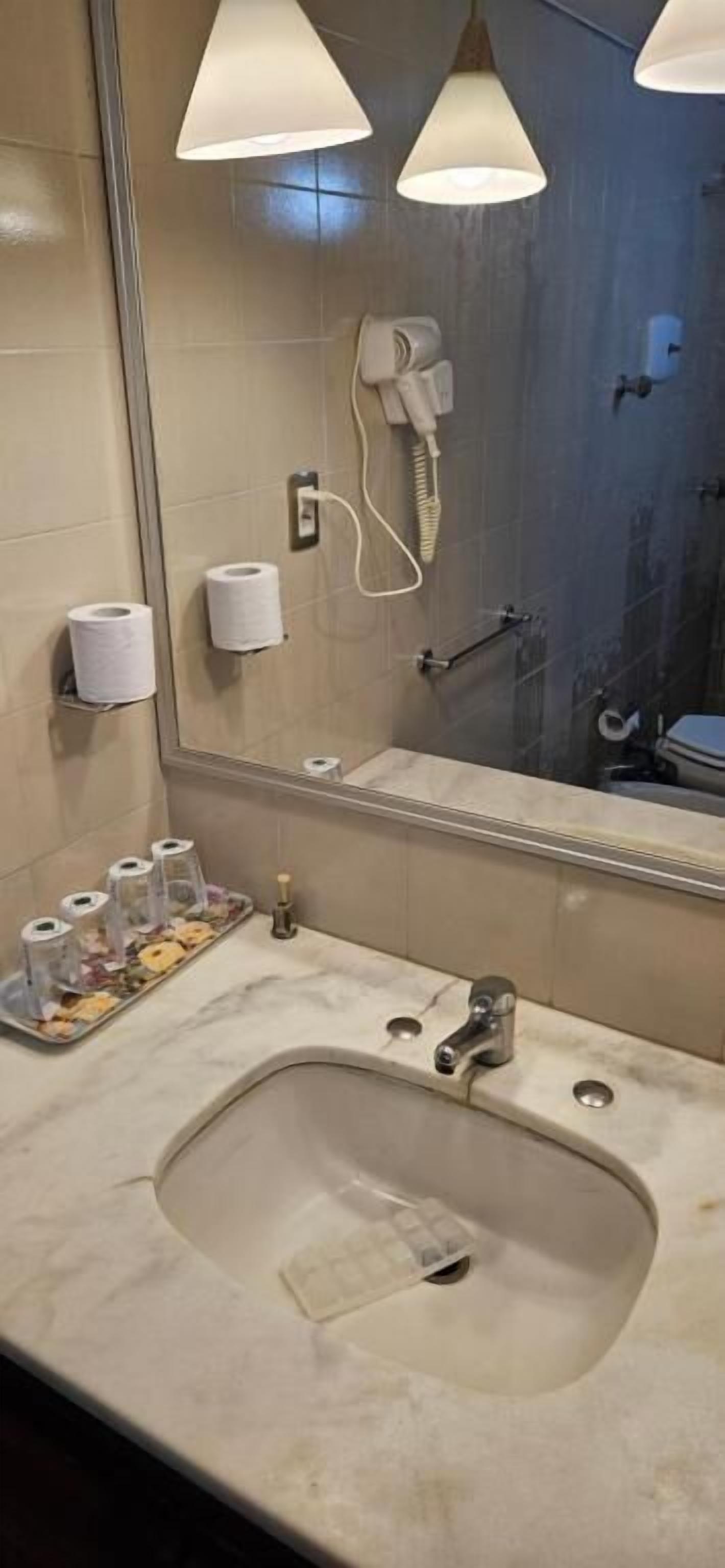 A bathroom with a sink, mirror, towel dispenser, and a hairdryer mounted on the wall.