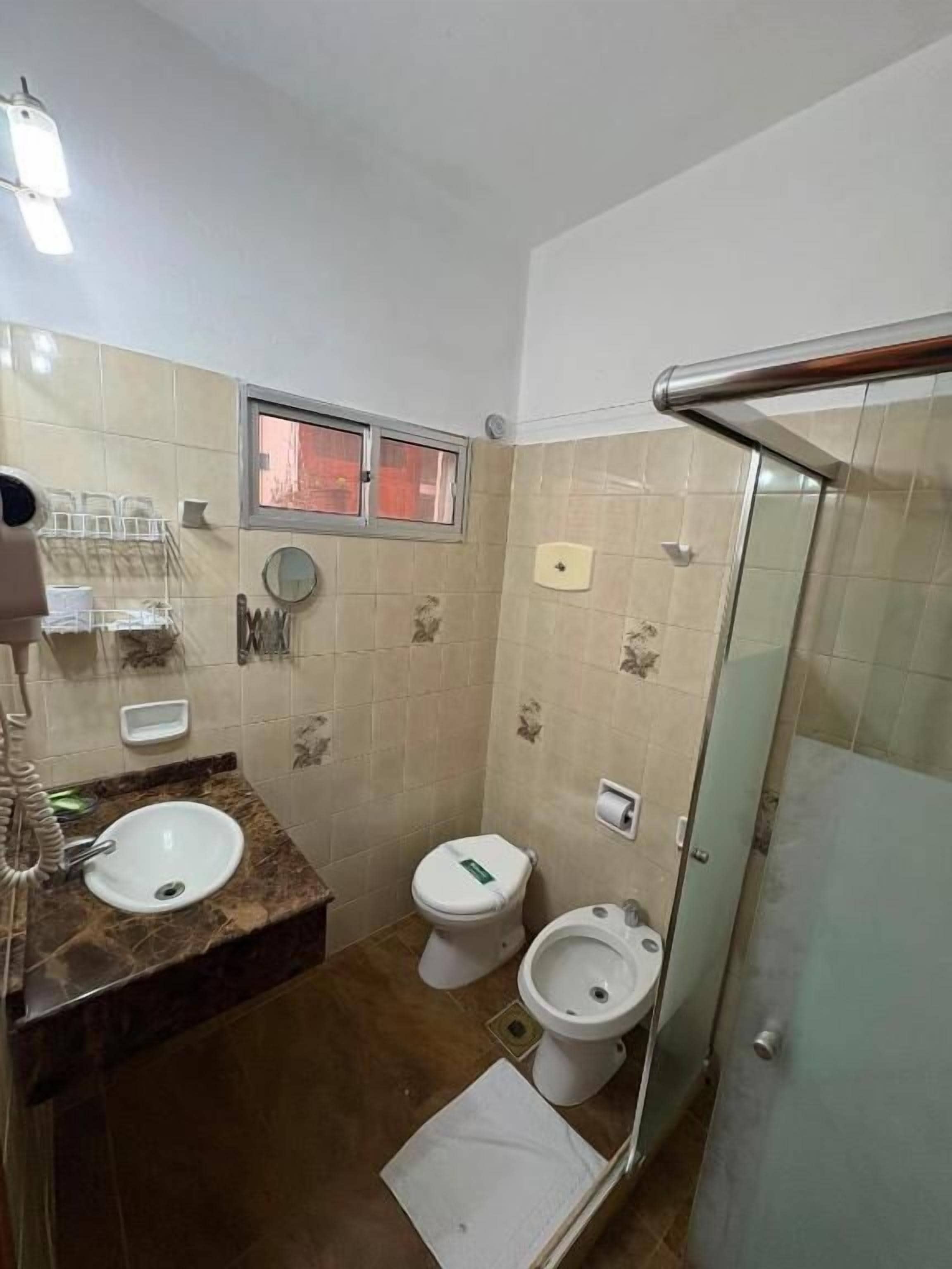 Een badkamer met een wastafel, twee toiletten, een douche en een douchecabine met glazen wanden.