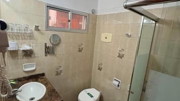 Een badkamer met een wastafel, twee toiletten, een douche en een douchecabine met glazen wanden.