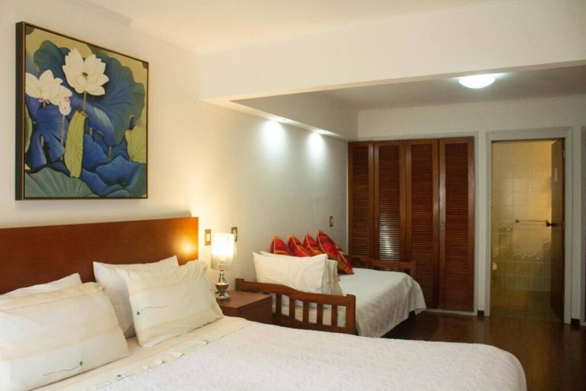 A hotel room with two beds, a painting of flowers, a wooden wardrobe, and a door leading to a balcony.