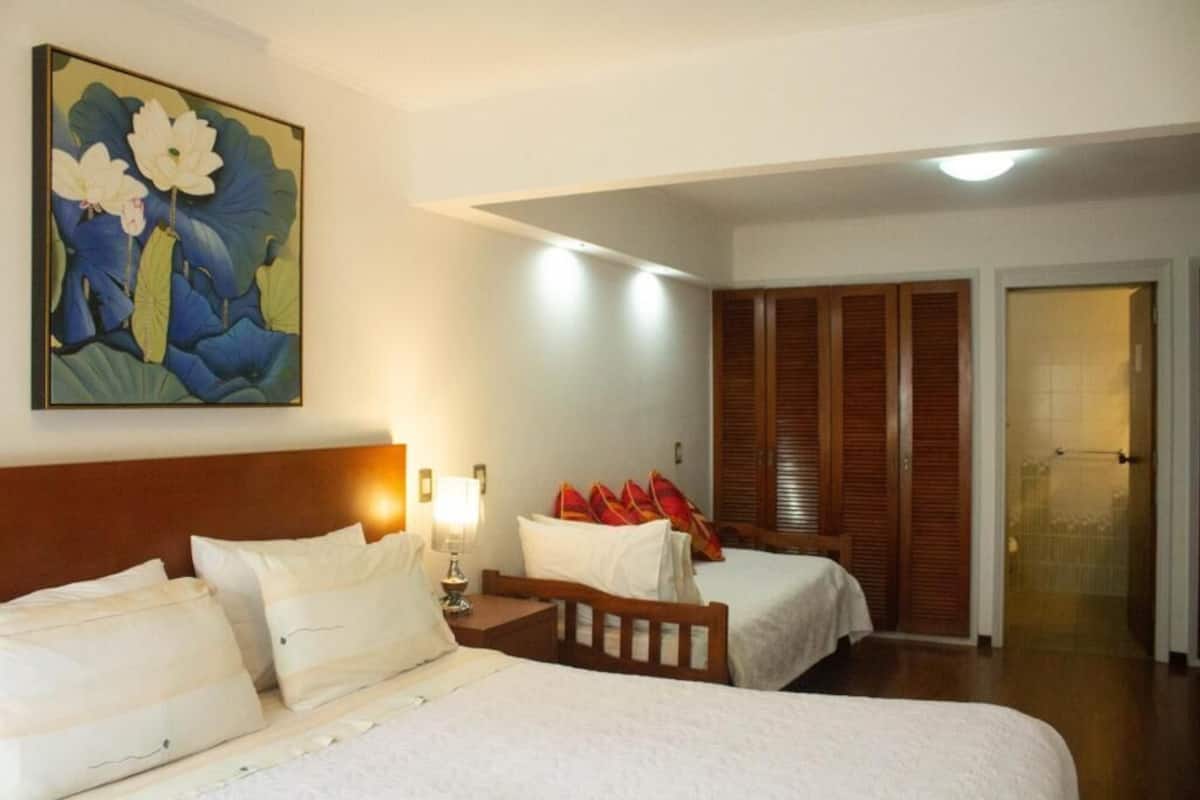 Habitación de hotel con dos camas, un cuadro de flores, un armario de madera y una puerta que da a un balcón.