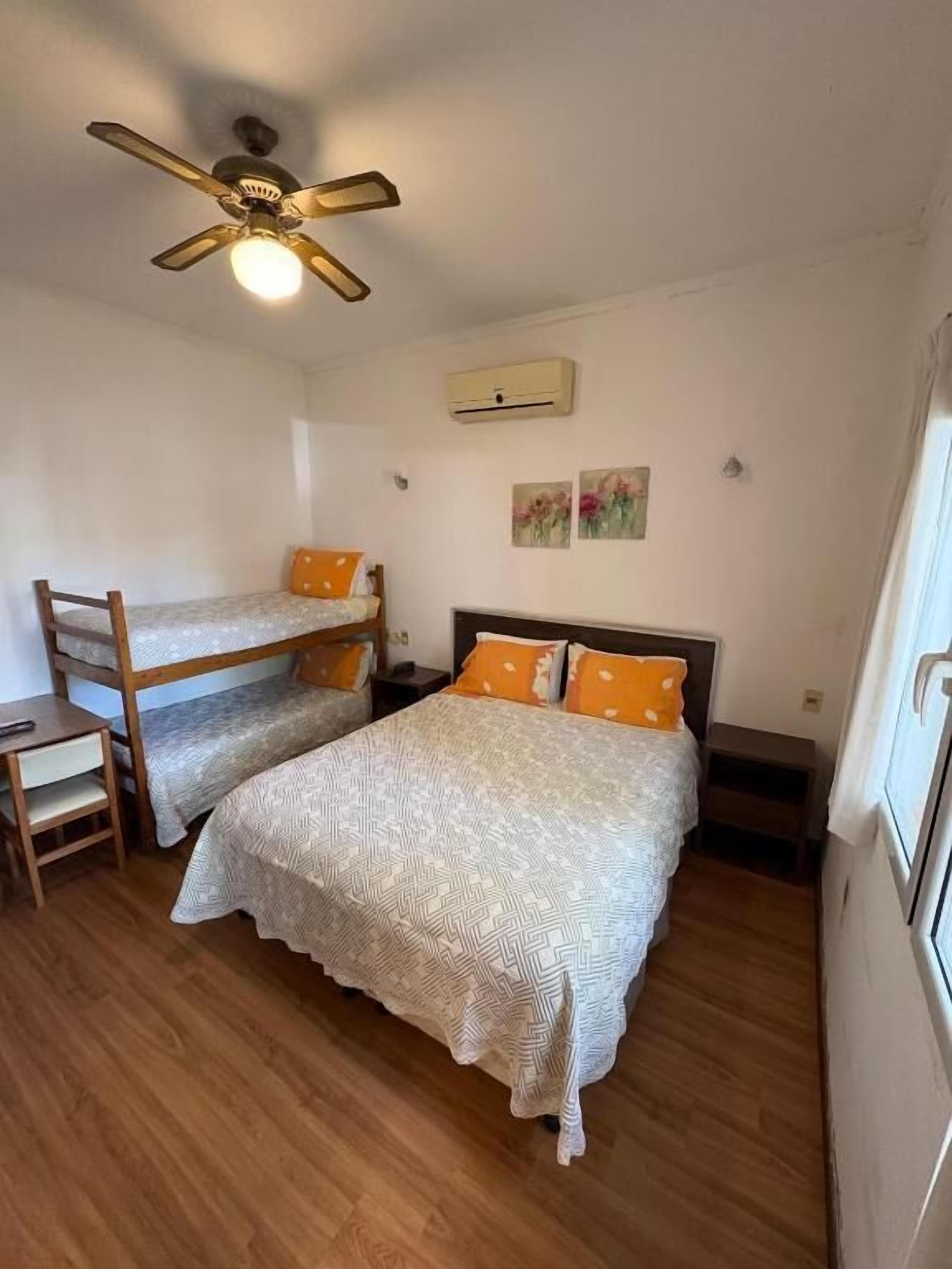 A bedroom with two beds, a ceiling fan, a small table, and a window.