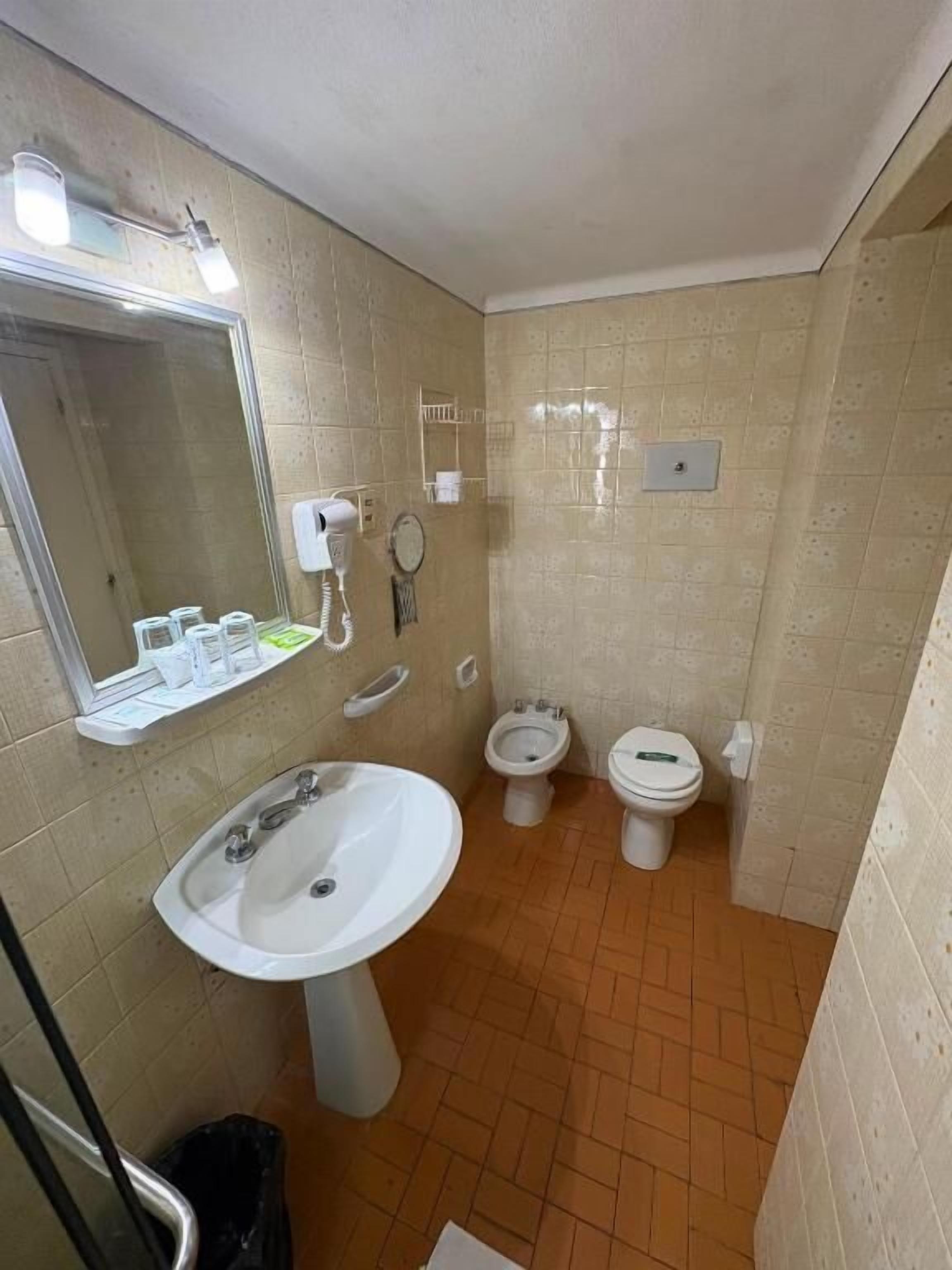 A bathroom with a sink, two toilets, a mirror, and a hairdryer.