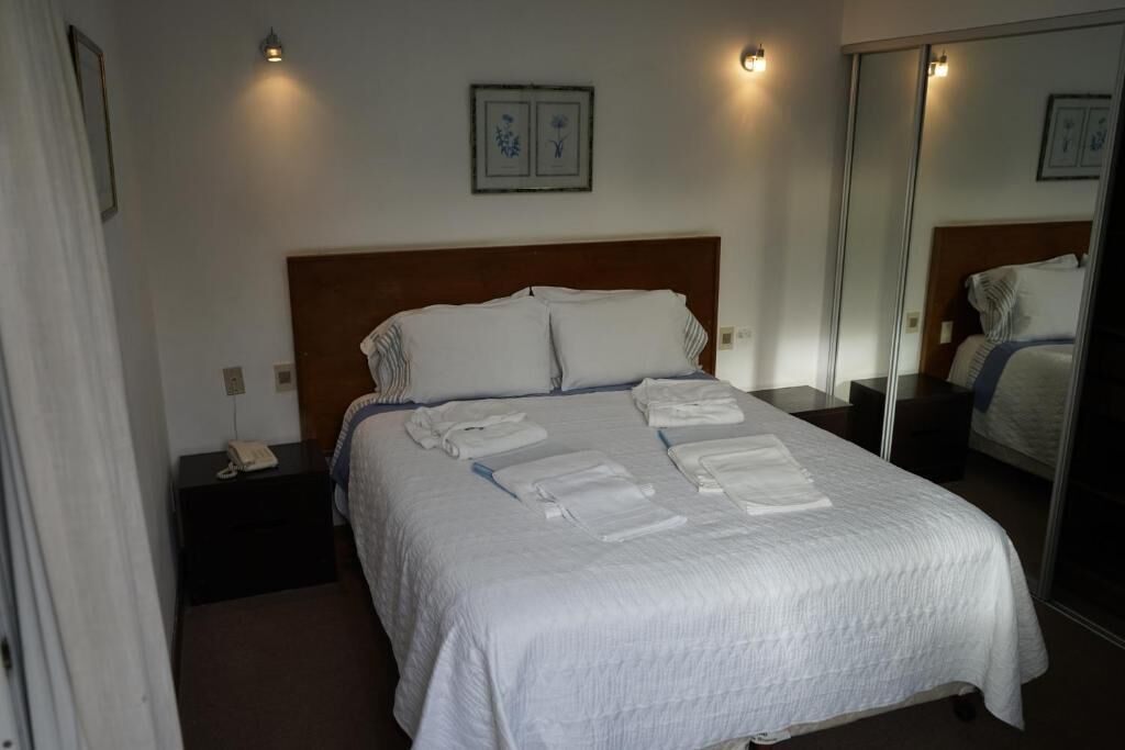 Una habitación de hotel con una cama grande, una mesita de noche con un teléfono y un espejo.