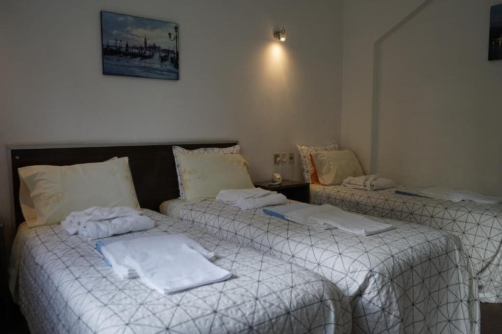 A hotel room with two beds, each with a geometric patterned bedspread, a nightstand with a lamp, and a painting on the wall.