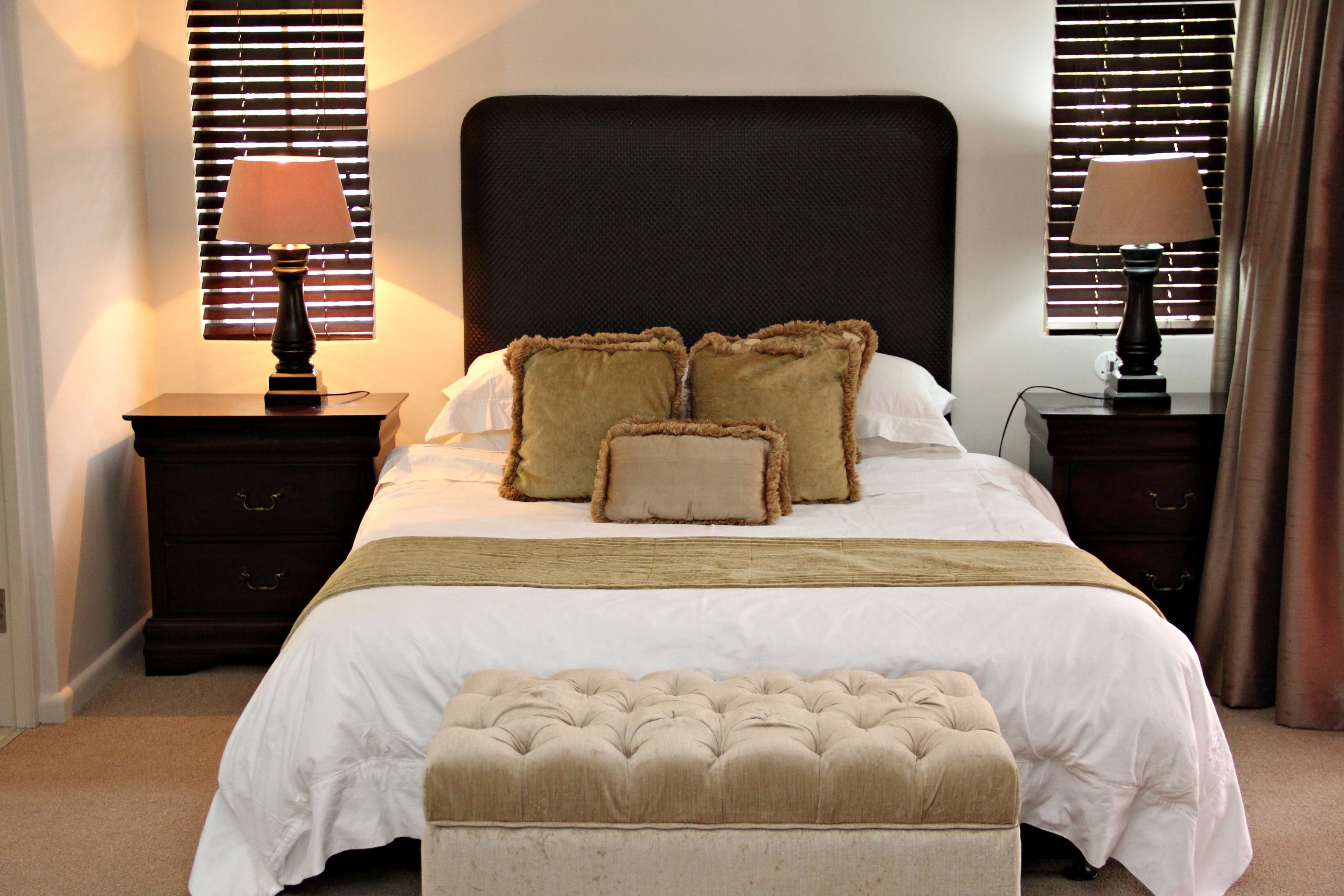 Un letto rifatto con un'elegante testiera imbottita, due comodini con lampade e un pouf coordinato.