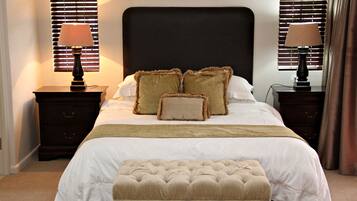 Un letto rifatto con un'elegante testiera imbottita, due comodini con lampade e un pouf coordinato.