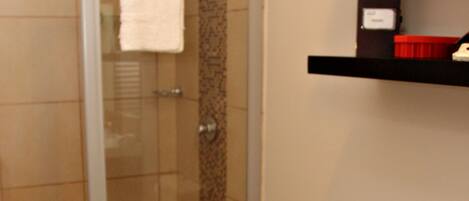 A bathroom with a glass shower enclosure, a toilet, and a shelf with toiletries.