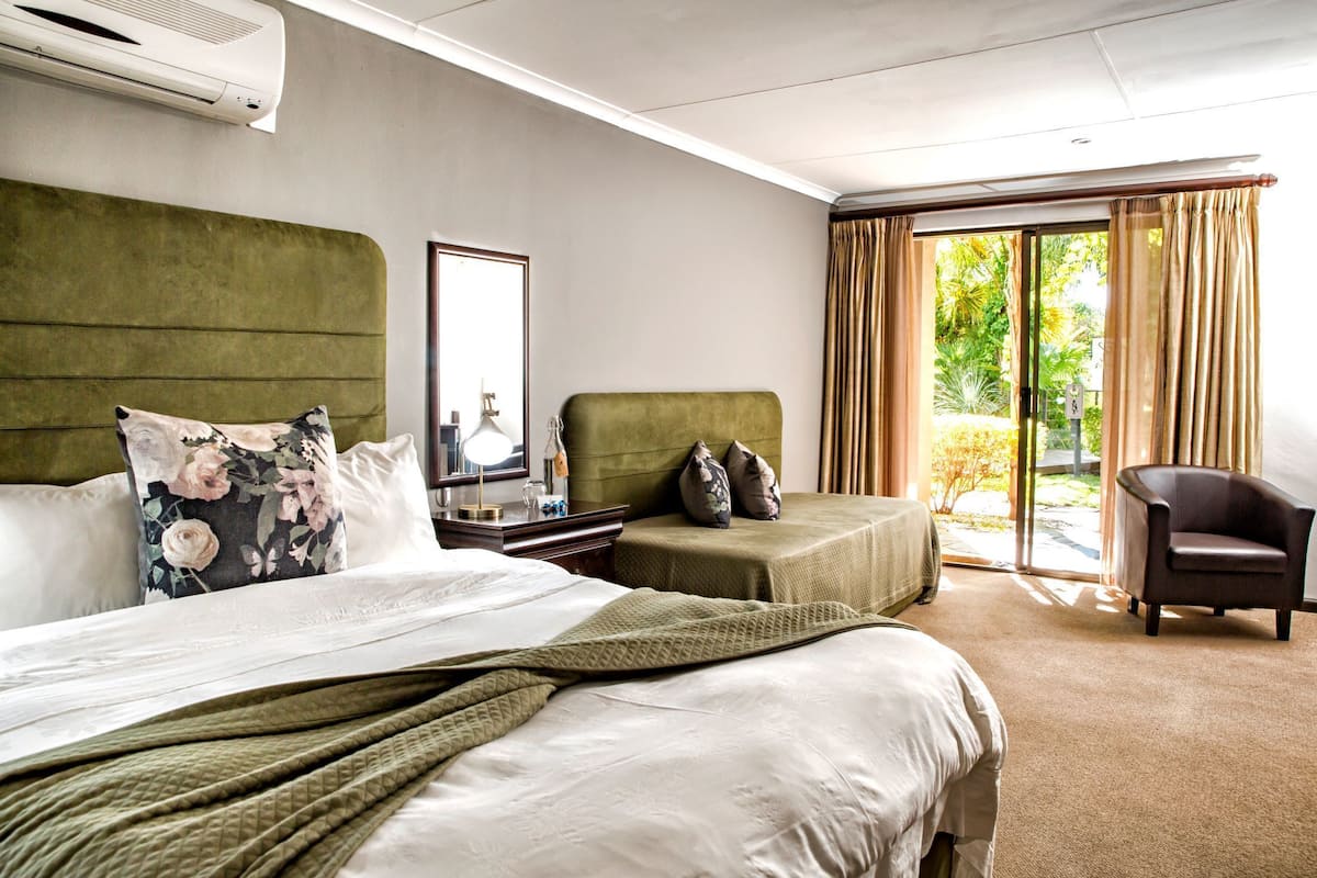Habitación de hotel con una cama grande, una cama más pequeña, una silla, un escritorio con espejo y vistas al exterior a través de una puerta corredera.