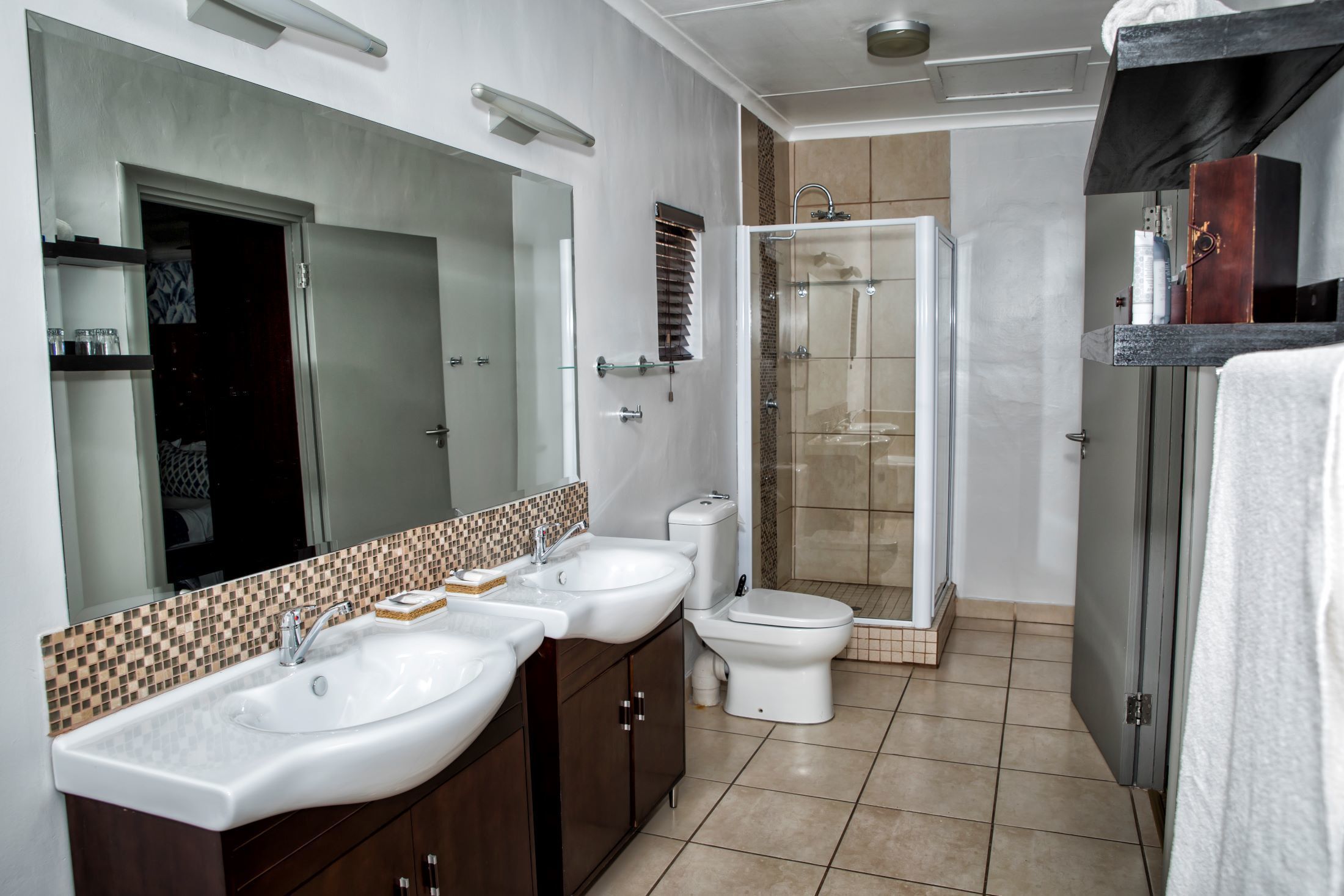 A modern bathroom with a double sink vanity, a toilet, and a glass-enclosed shower.
