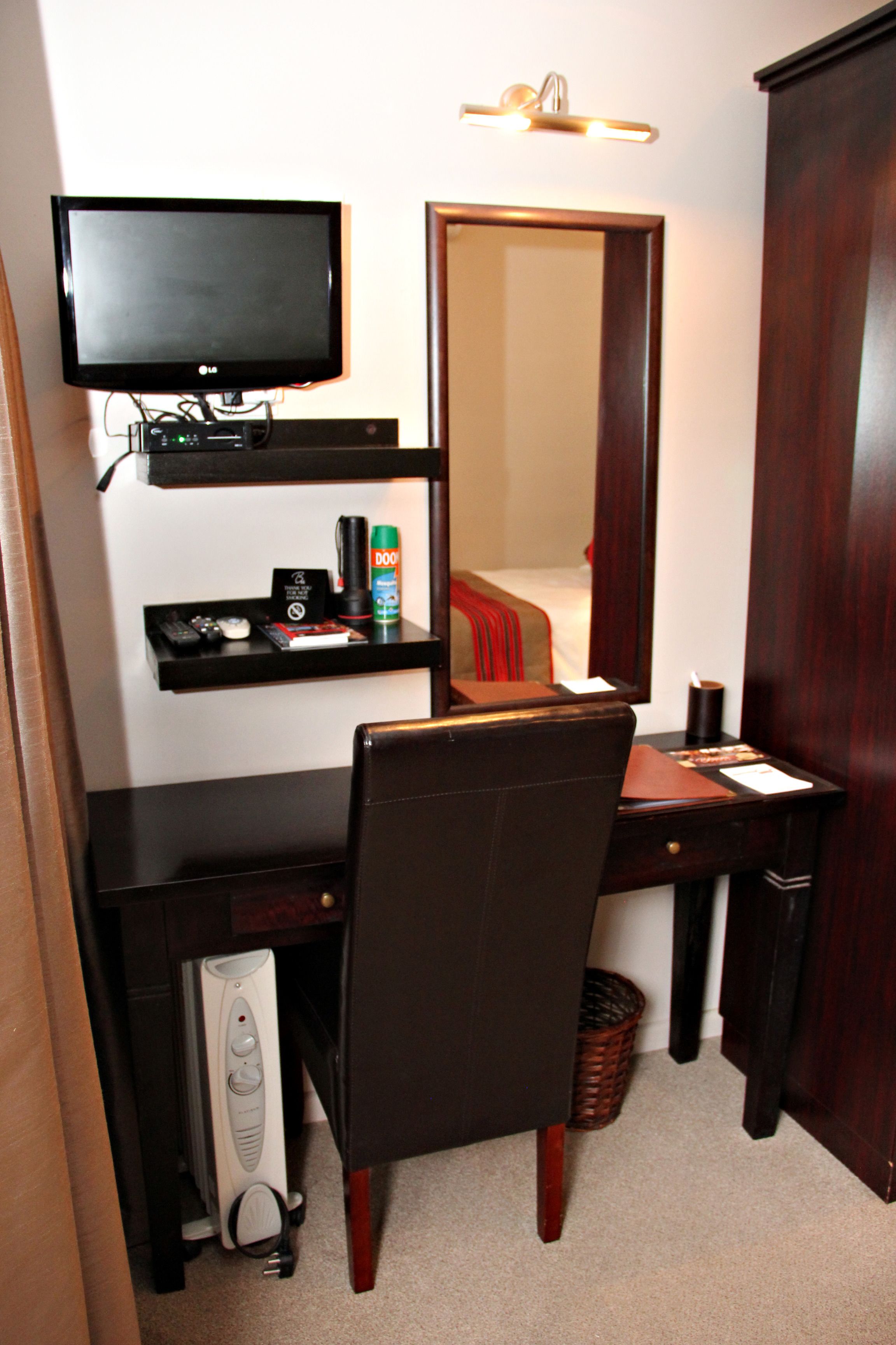Ein Hotelzimmer mit Schreibtisch, Stuhl, Computer, Fernseher und Spiegel.