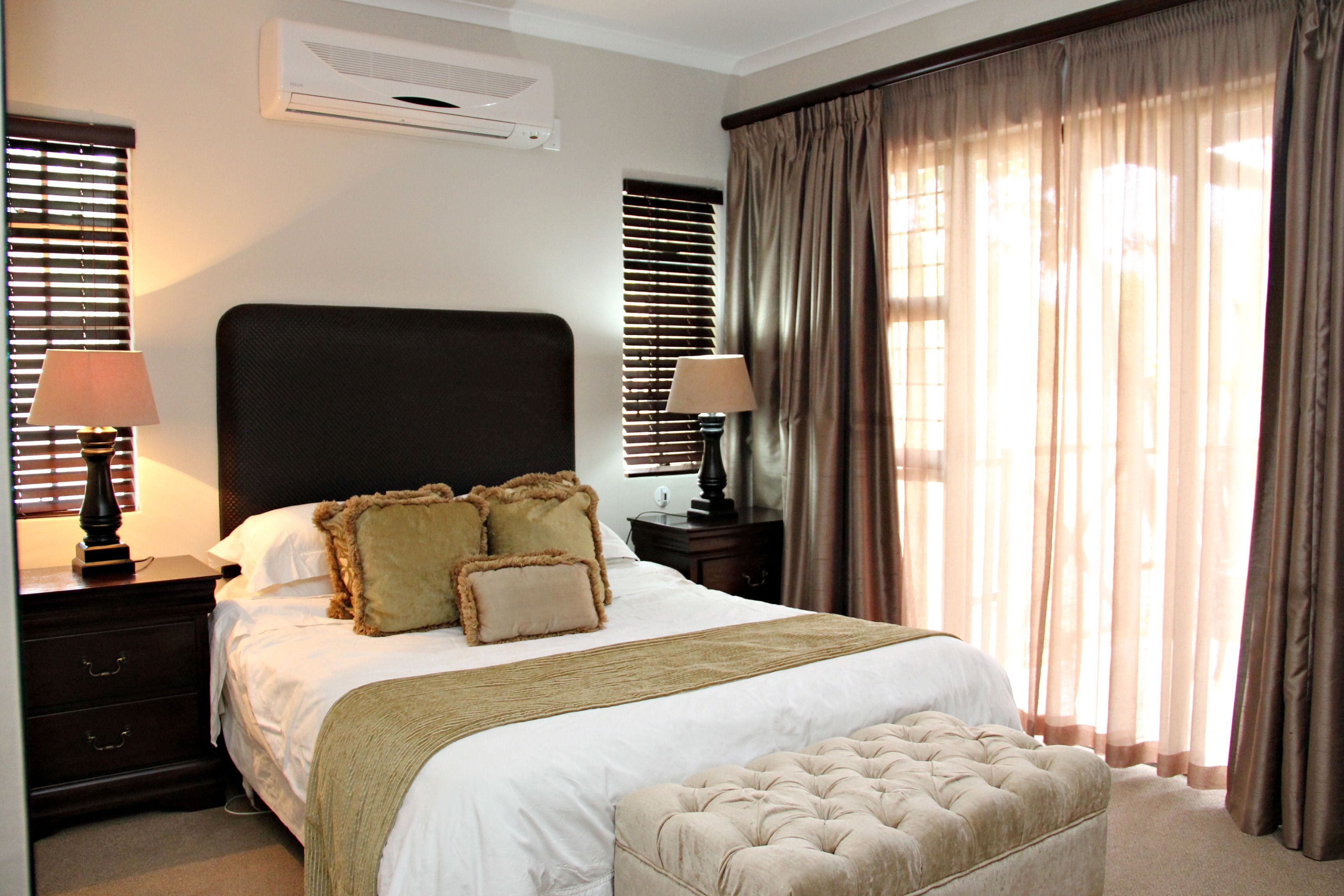 A neatly arranged bedroom with a large bed, a bedside table with lamps, a headboard, and a window with curtains.