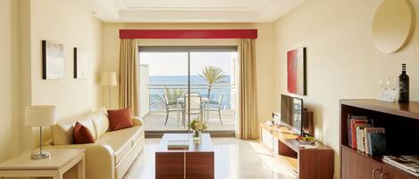 A modern hotel room with a balcony, a sofa, a coffee table, a TV, and a bookshelf.