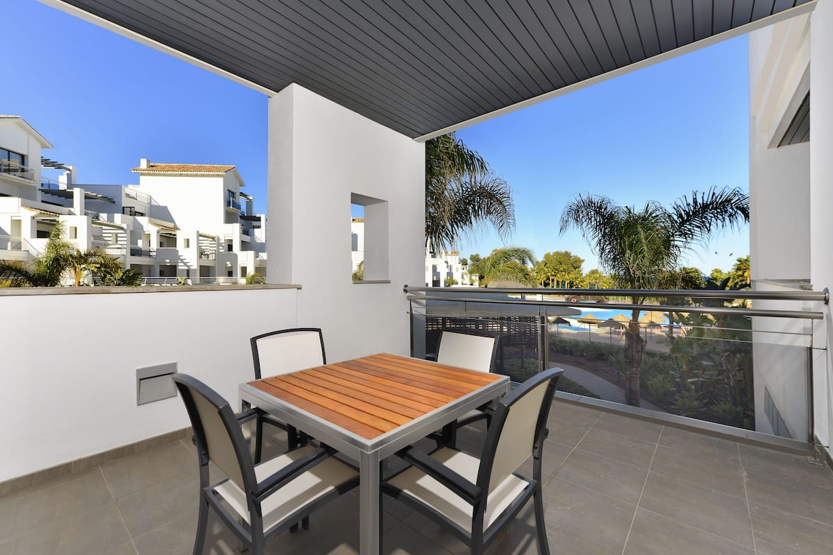 A balcony with a table and chairs, overlooking a pool and other buildings.