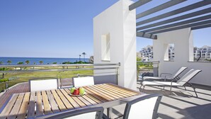 A balcony with a wooden table, white chairs, and a view of the ocean.