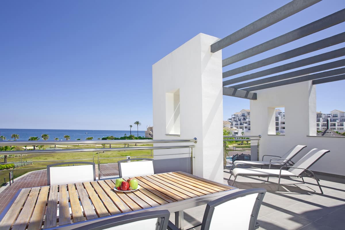 A balcony with a wooden table, white chairs, and a view of the ocean.