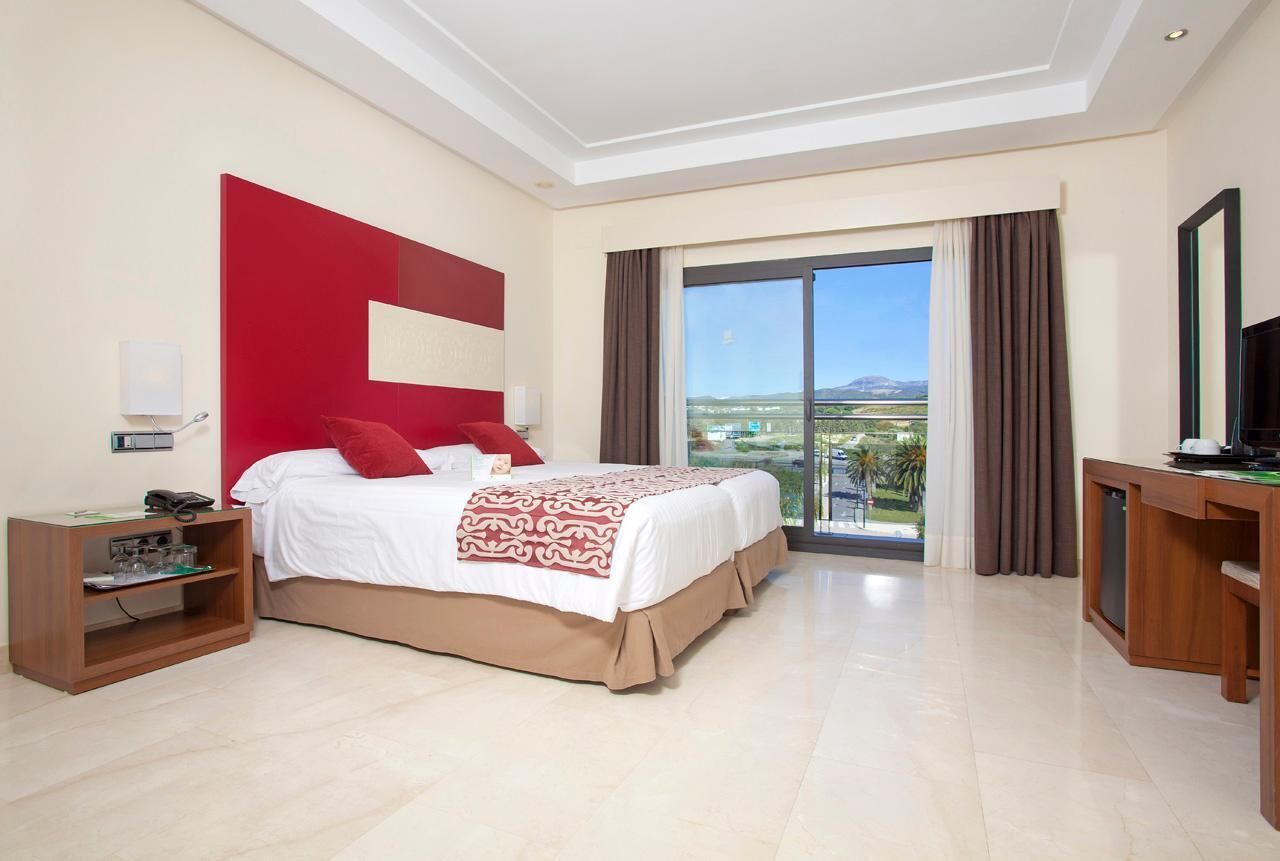 A hotel room with a large bed, a desk, a television, and a view of the outdoors.
