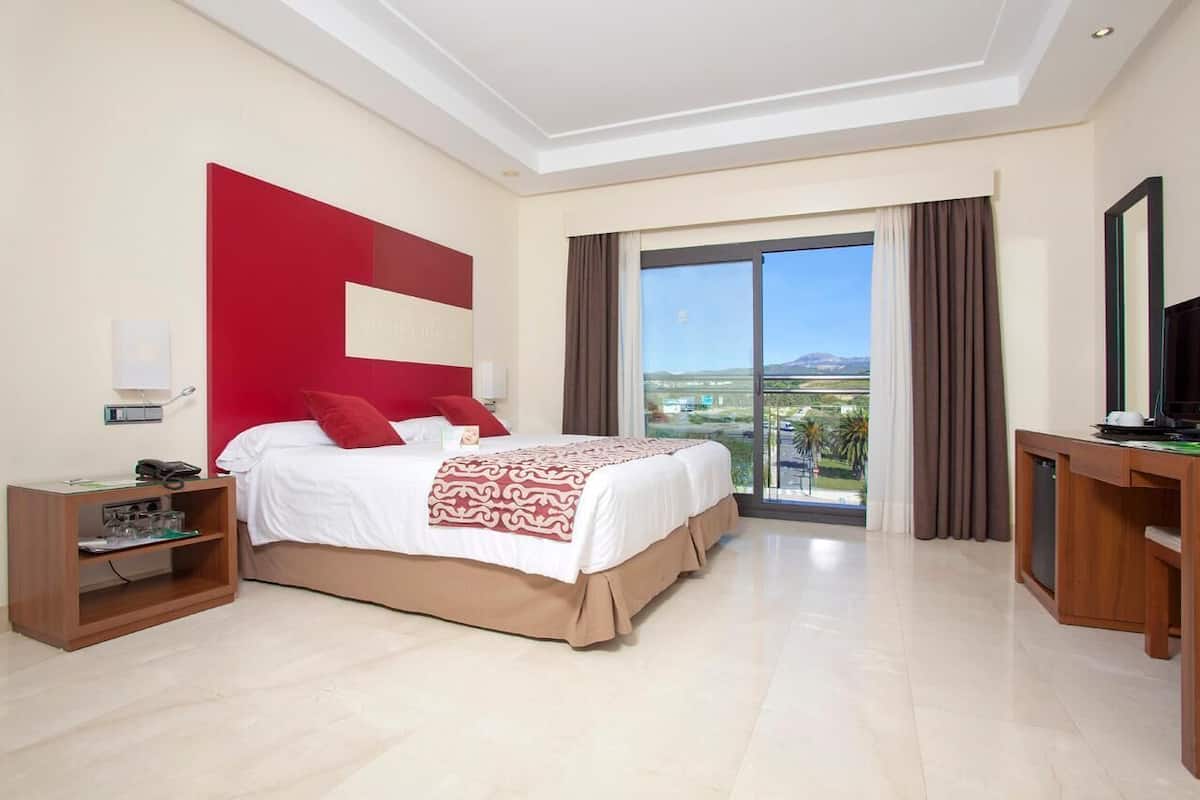 A hotel room with a large bed, a desk, a TV, and a view of the outdoors.
