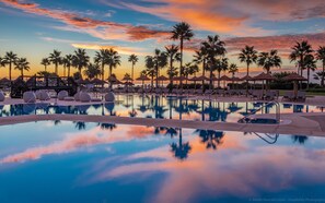 A poolside area with lounge chairs and umbrellas, surrounded by palm trees, reflecting a sunset sky. - Estepona Hotel & Spa Resort (Estepona)