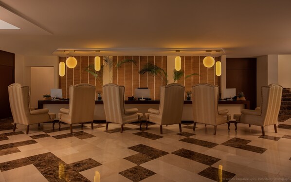 A hotel lobby with a checkered floor, leather armchairs, a reception desk, and a wall with vertical wooden slats and hanging spherical lights. - Estepona Hotel & Spa Resort (Estepona)