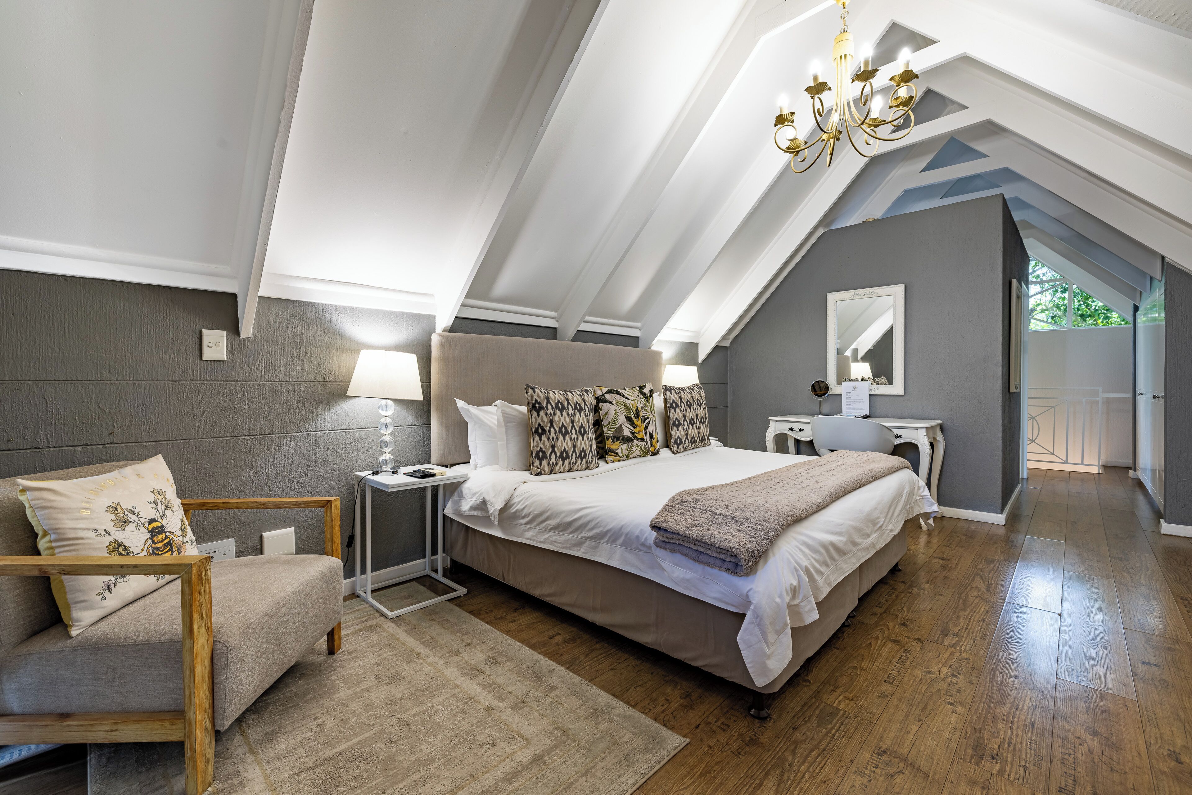 Quarto com uma cama grande, uma cadeira, uma mesa de cabeceira, um abajur e um candelabro.