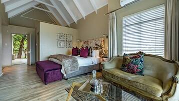 Ruime kamer met een groot bed, een bank en een glazen bijzettafeltje. Er is een raam met zonwering en een plafondventilator.