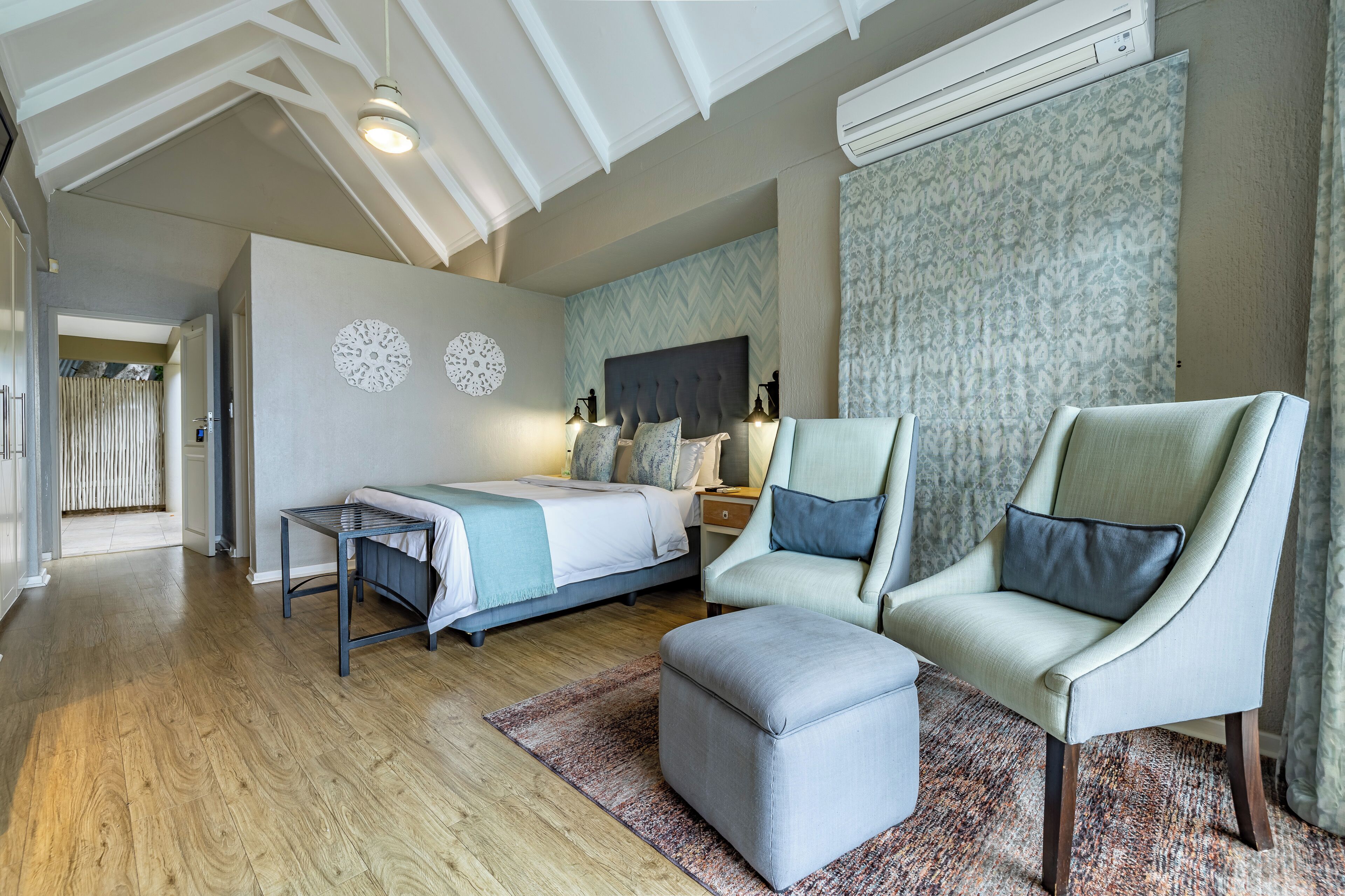 A spacious bedroom with a bed, two chairs, a table, and a large window with patterned curtains.