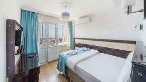 Habitación de hotel con cama, escritorio con computadora, televisor y ventana con cortinas.