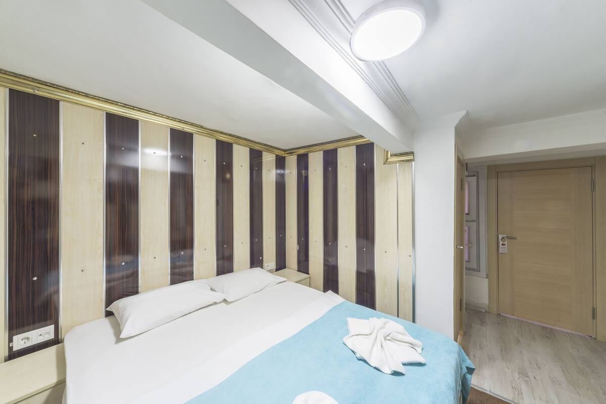 A hotel room with a bed, a nightstand, a wooden wardrobe, and a door.