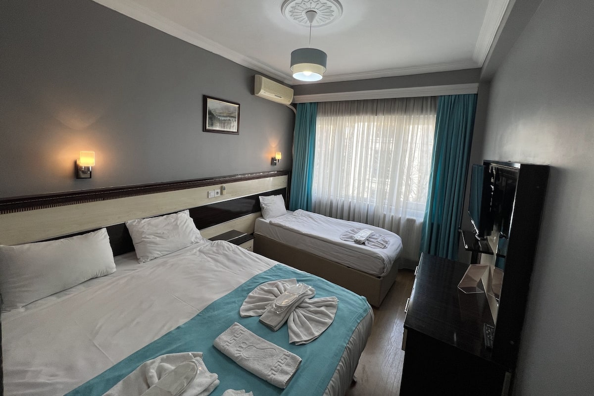 A hotel room with two beds, a ceiling fan, a TV, and a window with curtains.