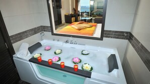 A modern bathroom with a large bathtub, a glass shower enclosure, and a view of a balcony with a table and chairs. - Hollywood Inn Hotel (Ghazir)