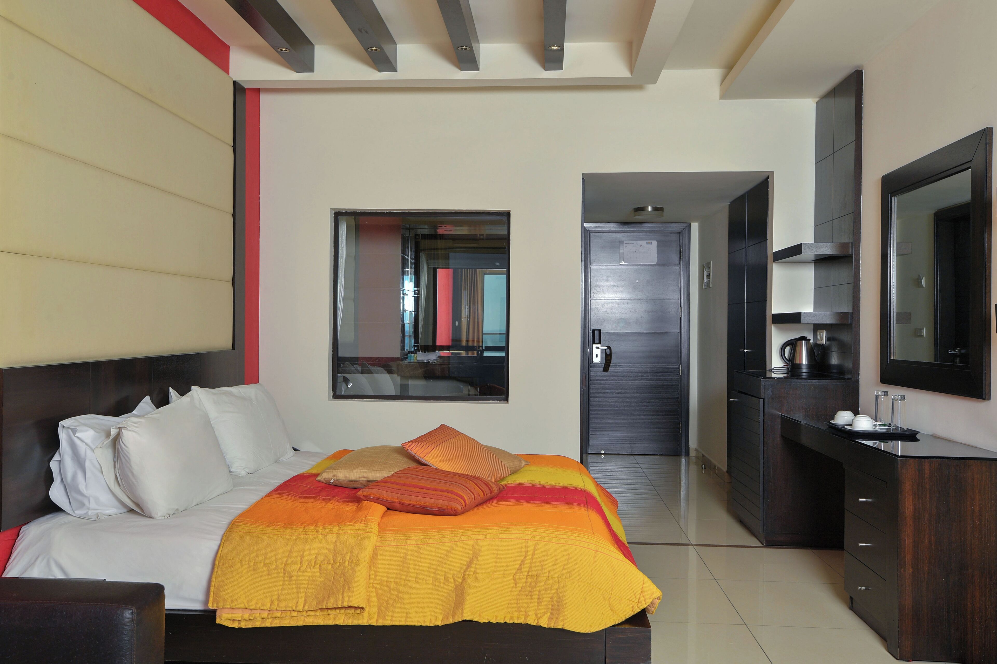 Ein modernes Hotelzimmer mit einem großen Bett, einem integrierten Schreibtisch, einem Spiegel und Blick auf den Flur.