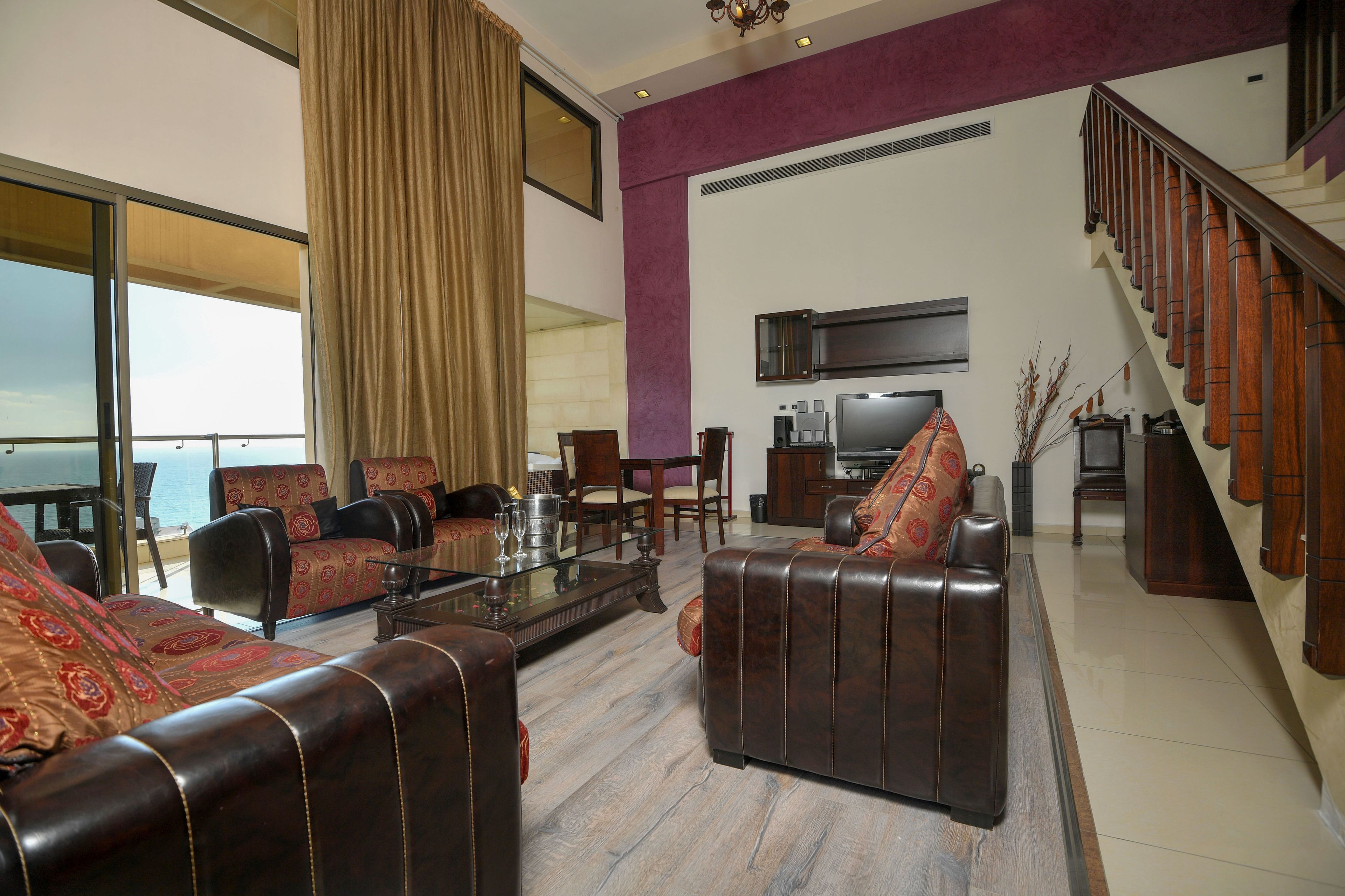 A spacious living room with leather sofas, a dining area, and a staircase.