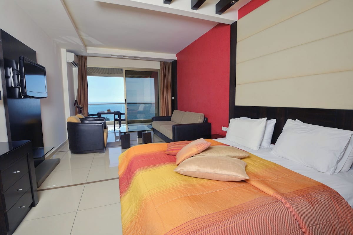 A hotel room with a bed, a TV, a sofa, and a balcony with a view.