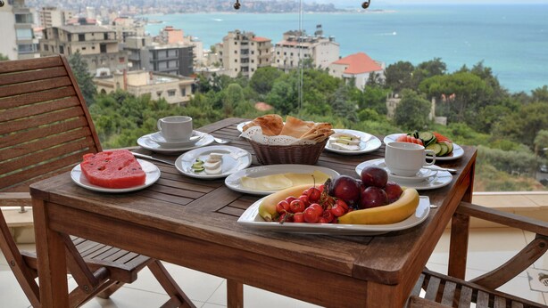 A balcony table with breakfast items and a view of the sea and cityscape. - Hollywood Inn Hotel (Ghazir)
