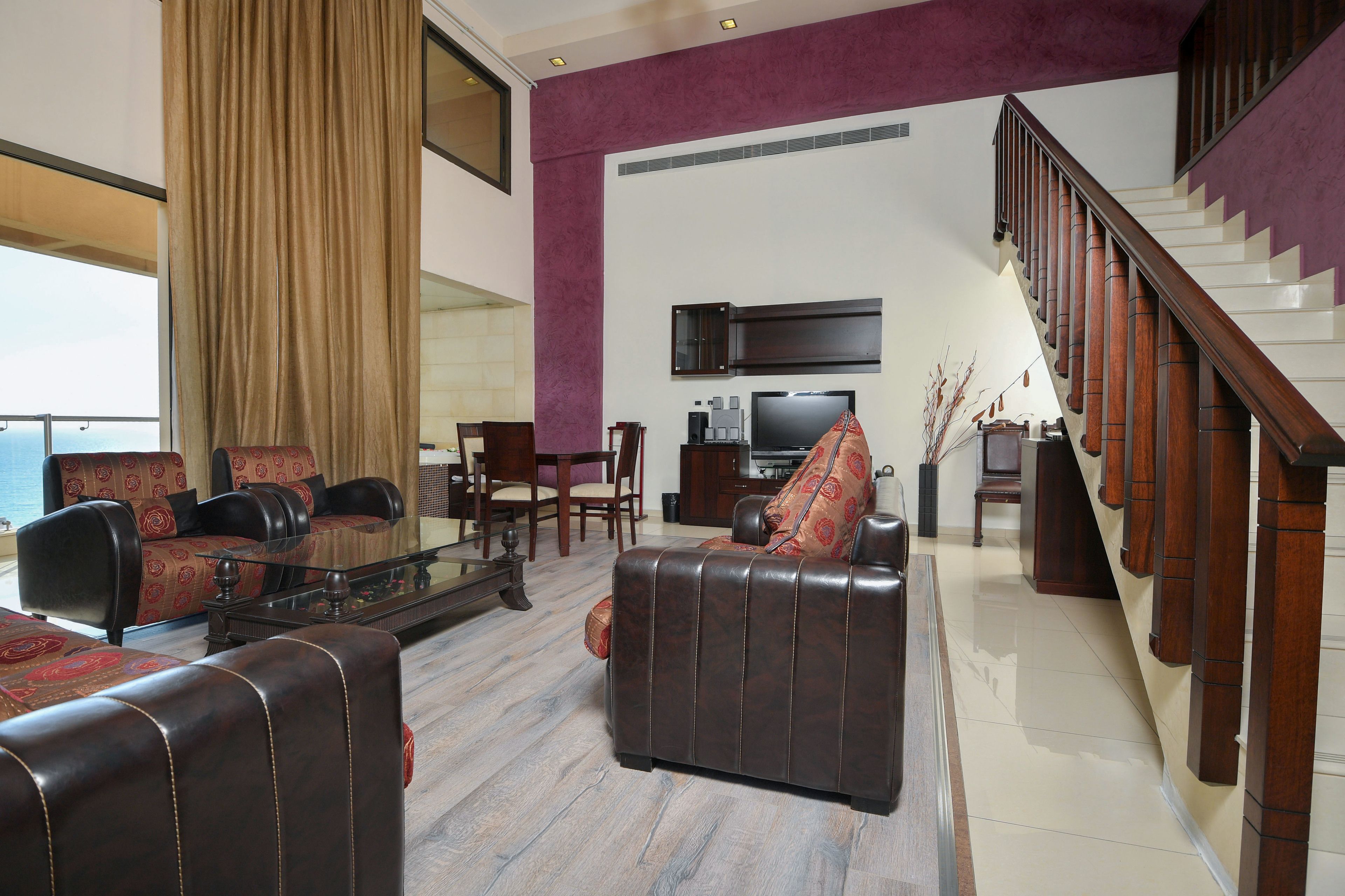A spacious living room with leather sofas, a coffee table, and a staircase leading to an upper floor.