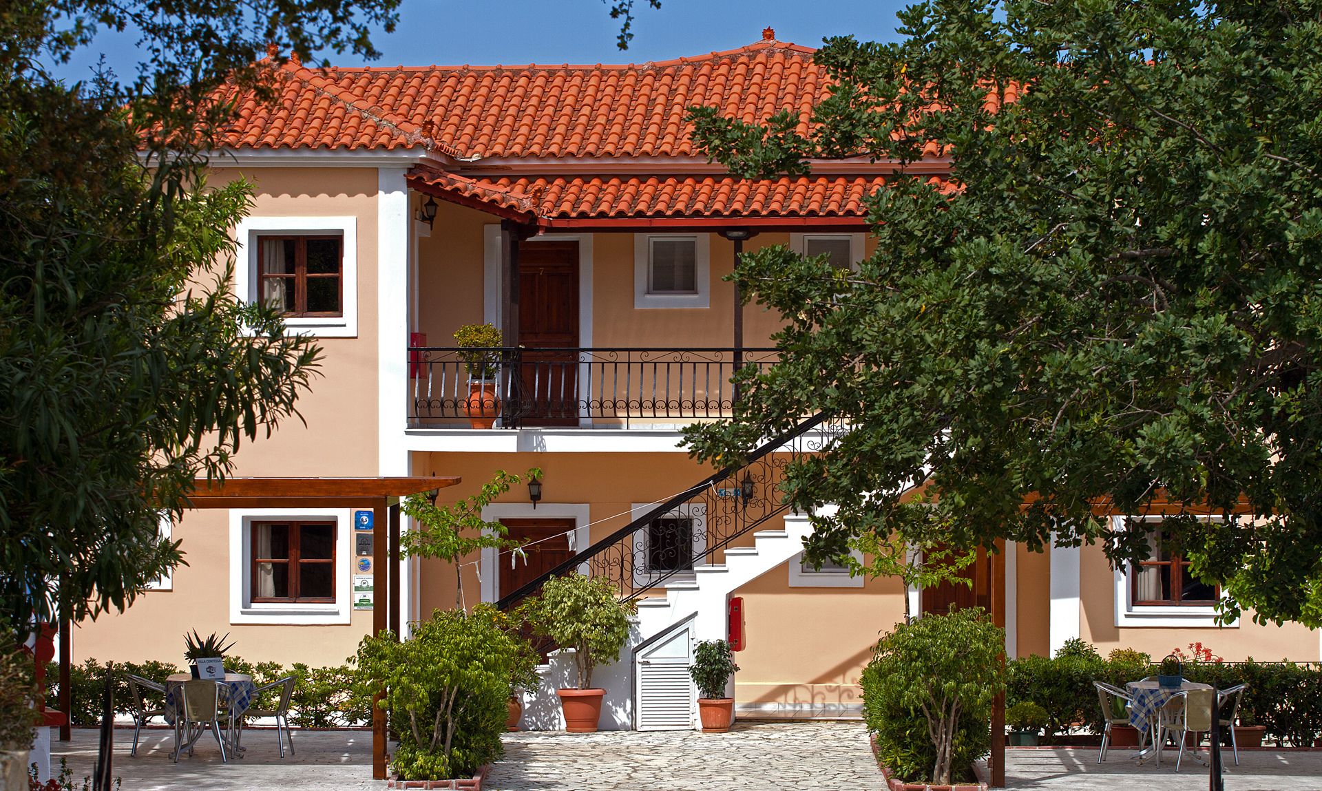 A two-story building with a red-tiled roof, a balcony, and a staircase leading to the upper floor.
