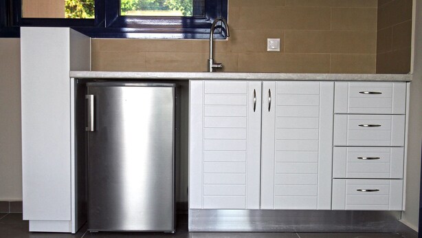 A kitchen with a stainless steel refrigerator, white cabinets, and a window above the sink. - Villa Contessa (Zakynthos)
