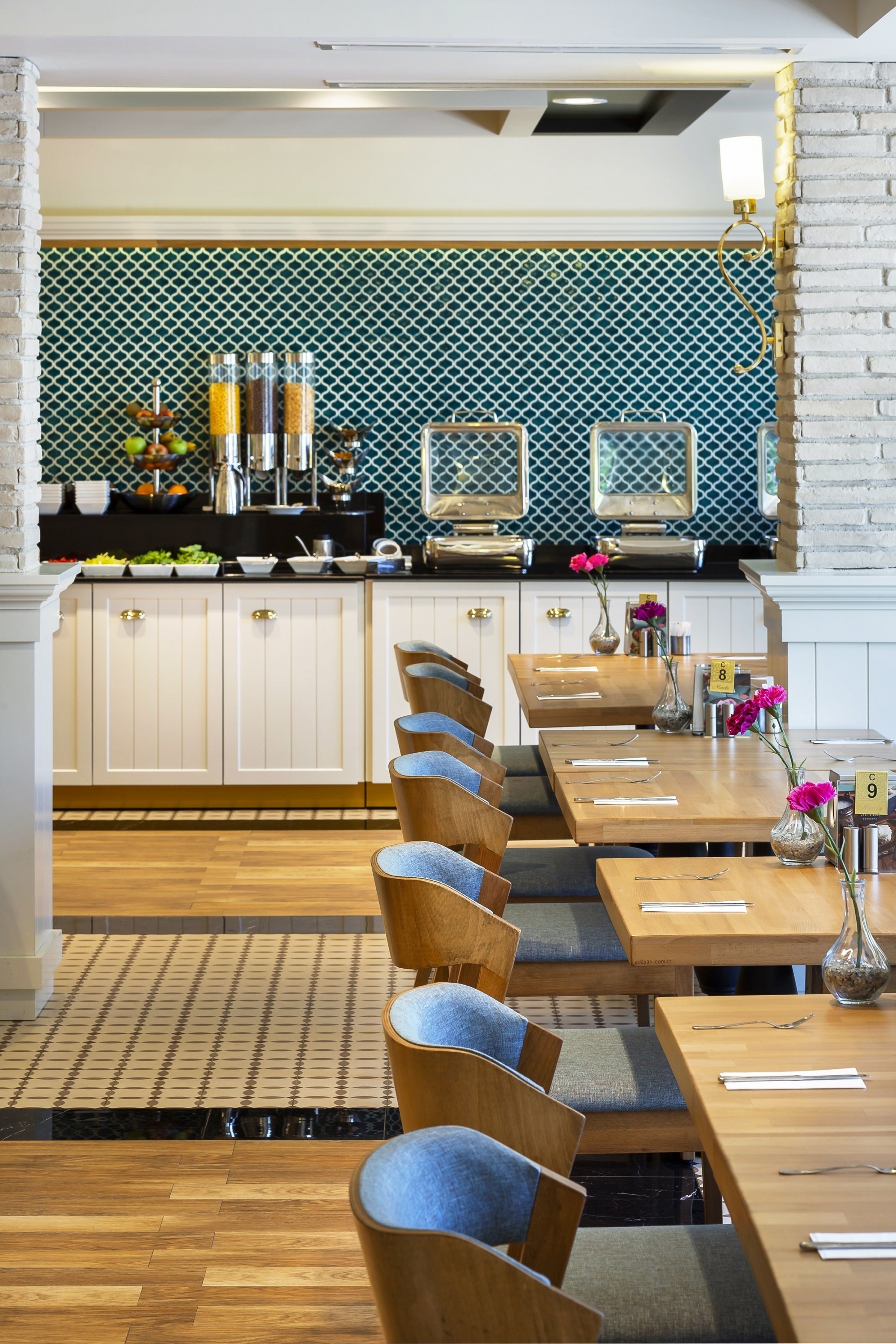 A restaurant with wooden tables and chairs, a tiled backsplash, and a brick accent wall.