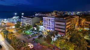 A multi-story hotel with a prominent sign, a parking area, and a view of the cityscape. - Artur Hotel (Çanakkale)