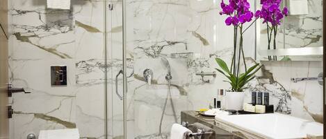 A modern bathroom with a glass-enclosed shower, a marble-tiled floor, a wooden vanity, and a large mirror.