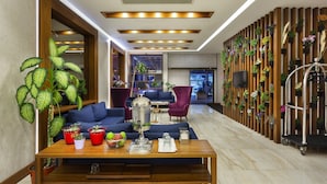 A modern hotel lobby with a wooden reception desk, blue sofas, and a wall-mounted planter with various plants. - Artur Hotel (Çanakkale)