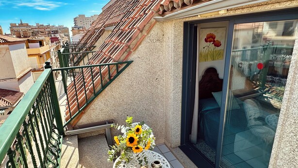 A balcony with a tiled roof, a table with a floral arrangement and pastries, and a view of the cityscape. - Hotel Reyesol (Fuengirola)