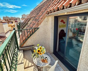 A balcony with a tiled roof, a table with a floral arrangement and pastries, and a view of the cityscape. - Hotel Reyesol (Fuengirola)