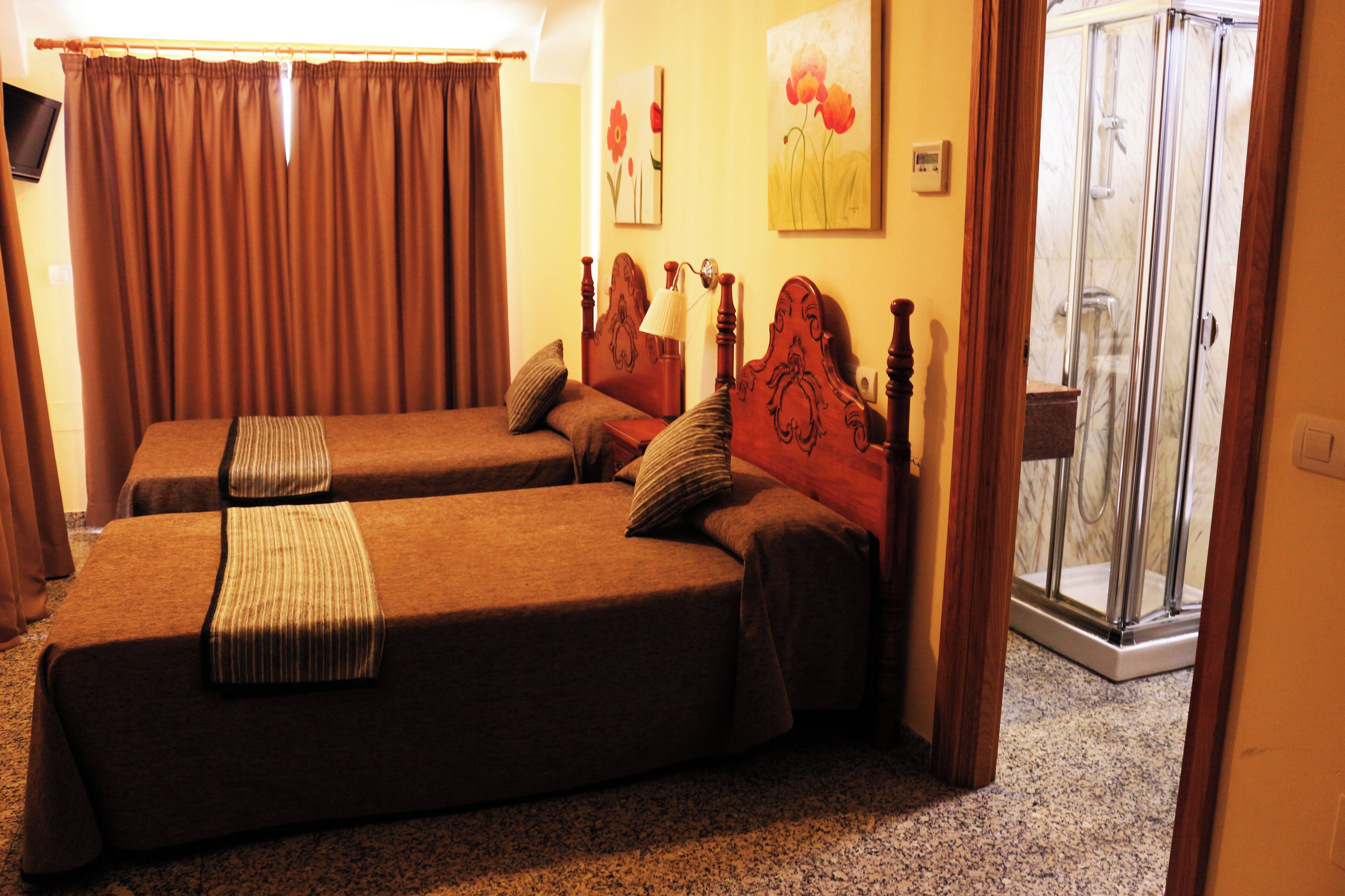 A hotel room with two single beds, a shower area, and a television on the wall.