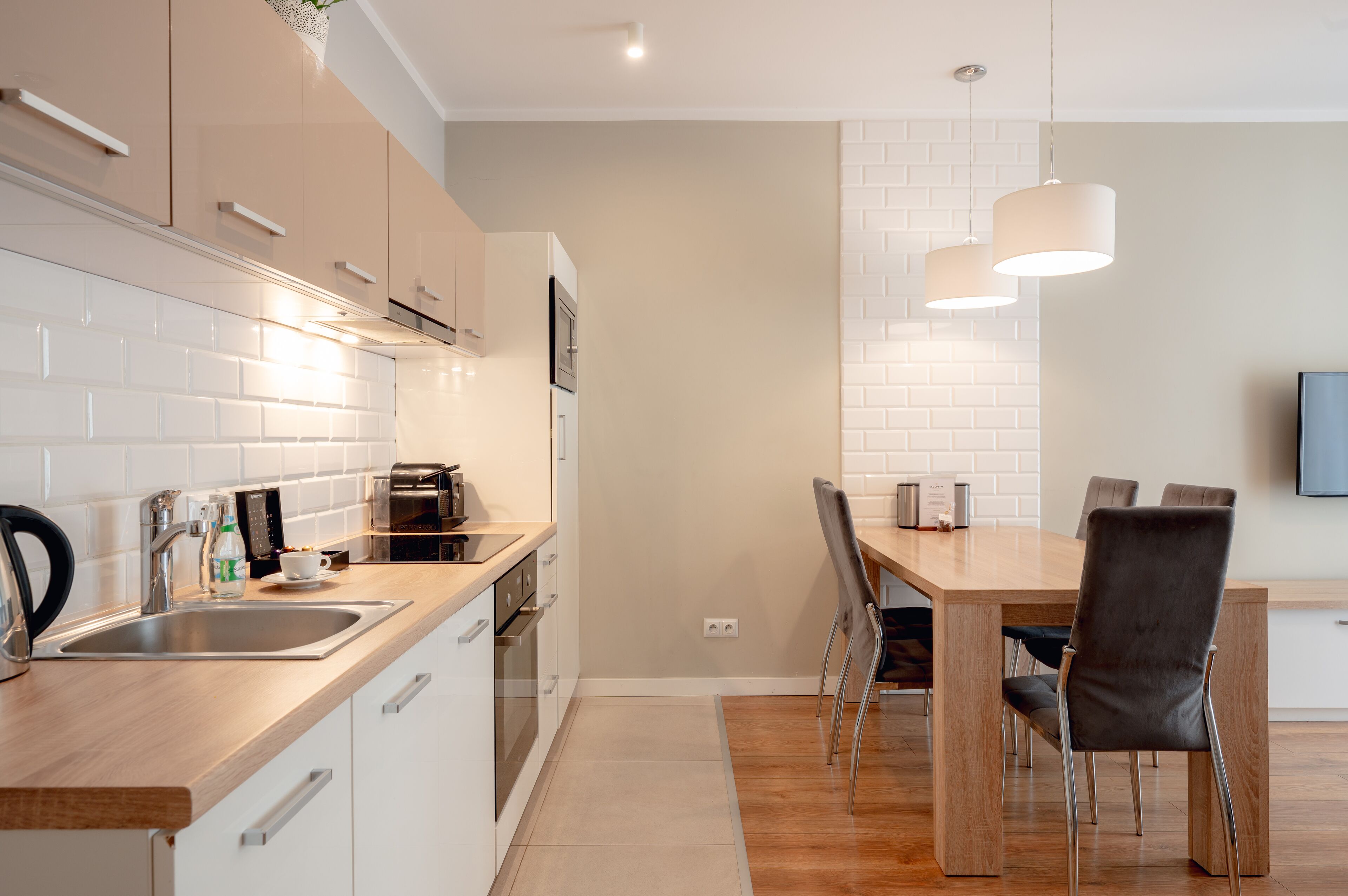 A modern kitchen with white cabinets, a stainless steel sink, and a wooden dining table with chairs.